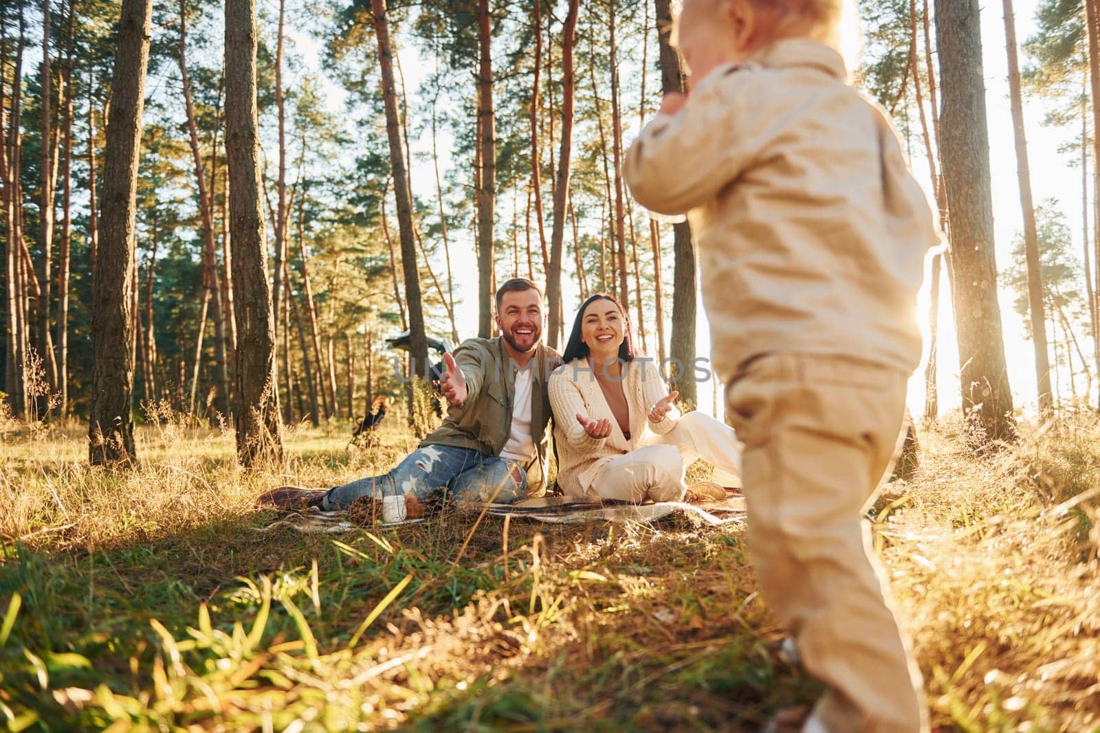 Little girl is running. Happy family of father, mother and little daughter is in the forest by Standret