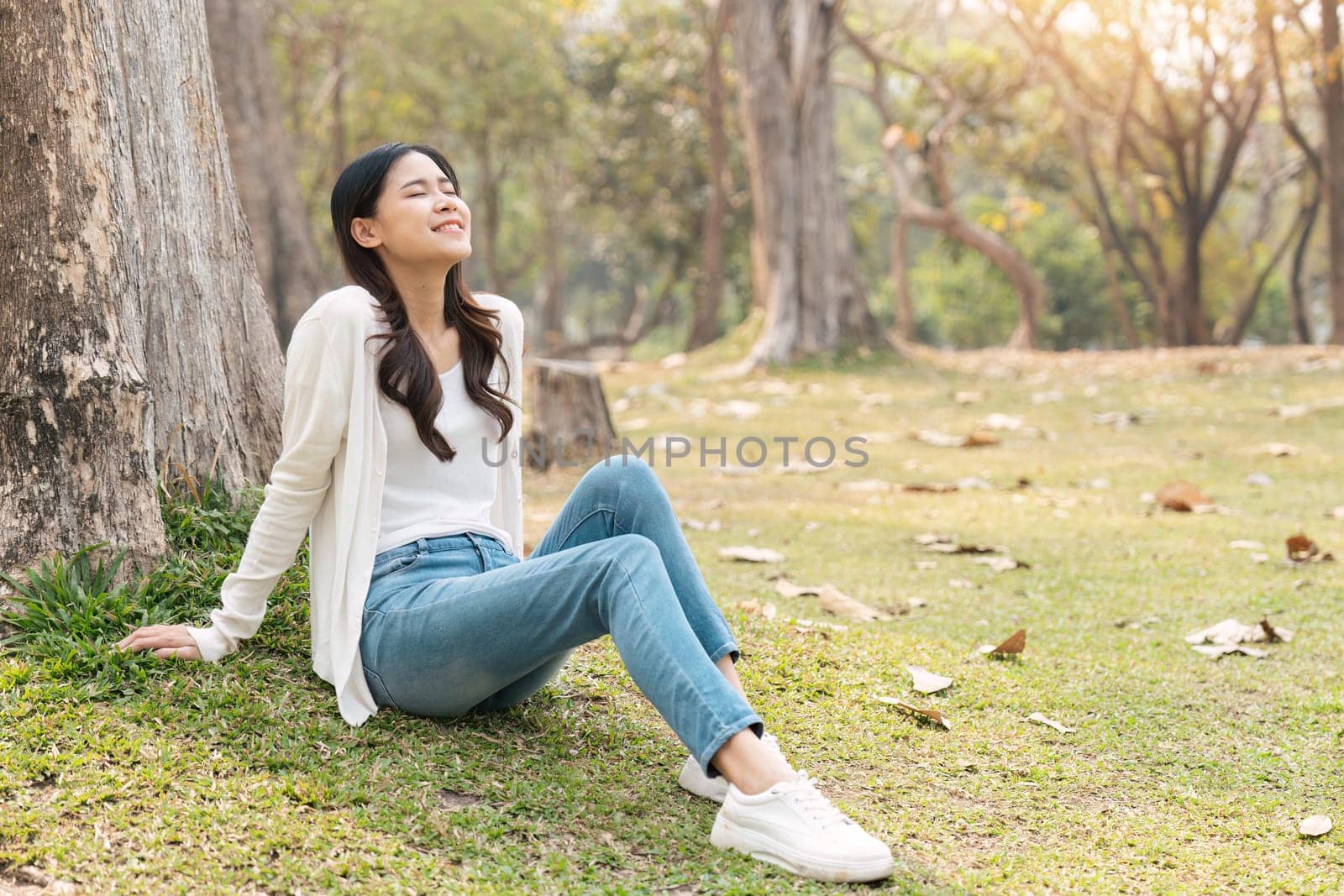 happy Asian woman sitting on grass in the green park, relaxing with nature in the park.