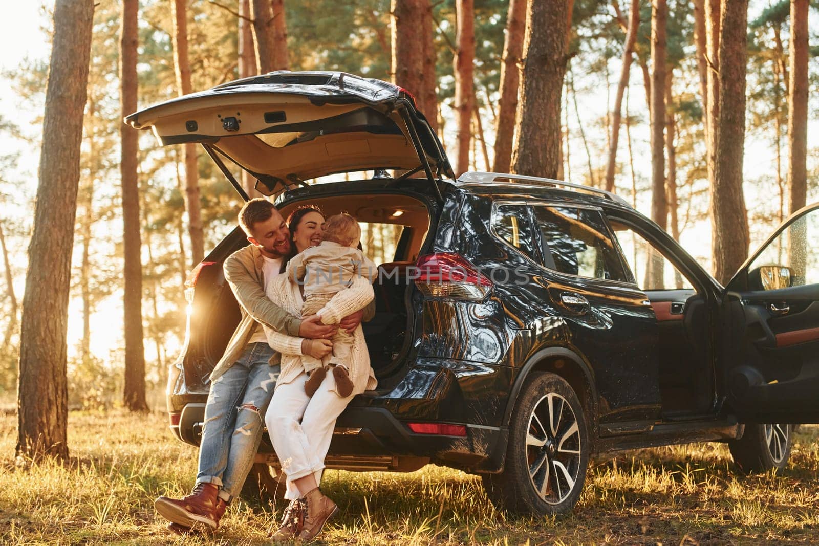 Leaning on the car. Happy family of father, mother and little daughter is in the forest.
