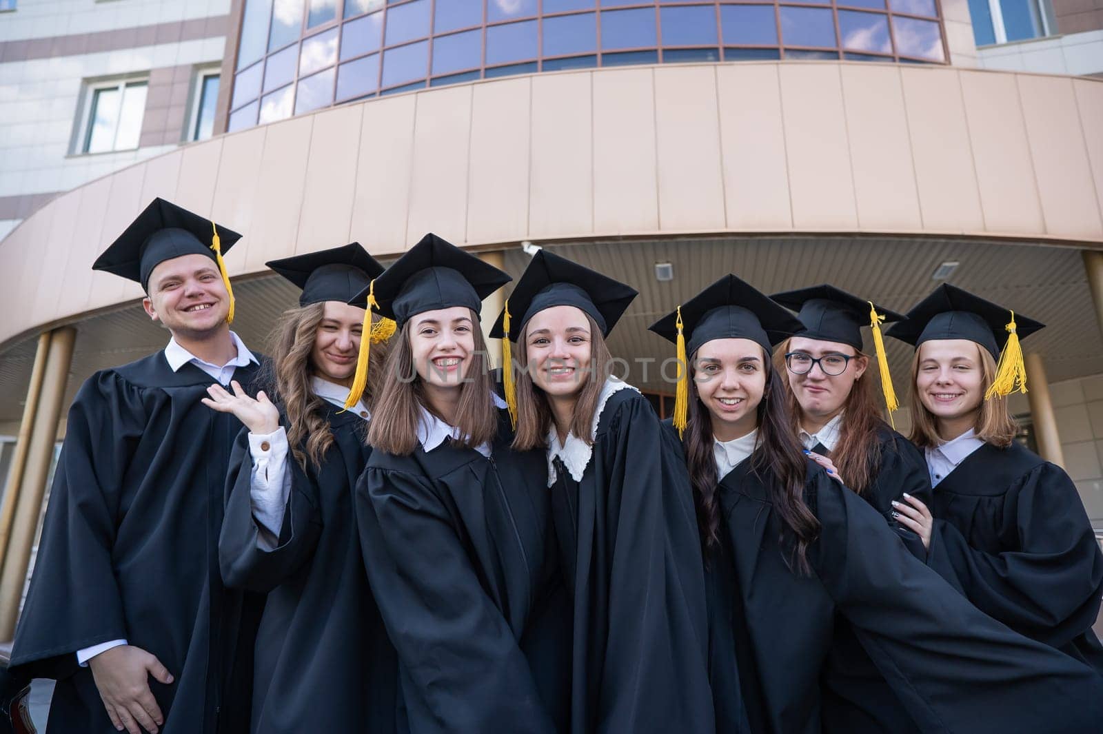 Happy students in graduate gown stand in a row against the backdrop of the university