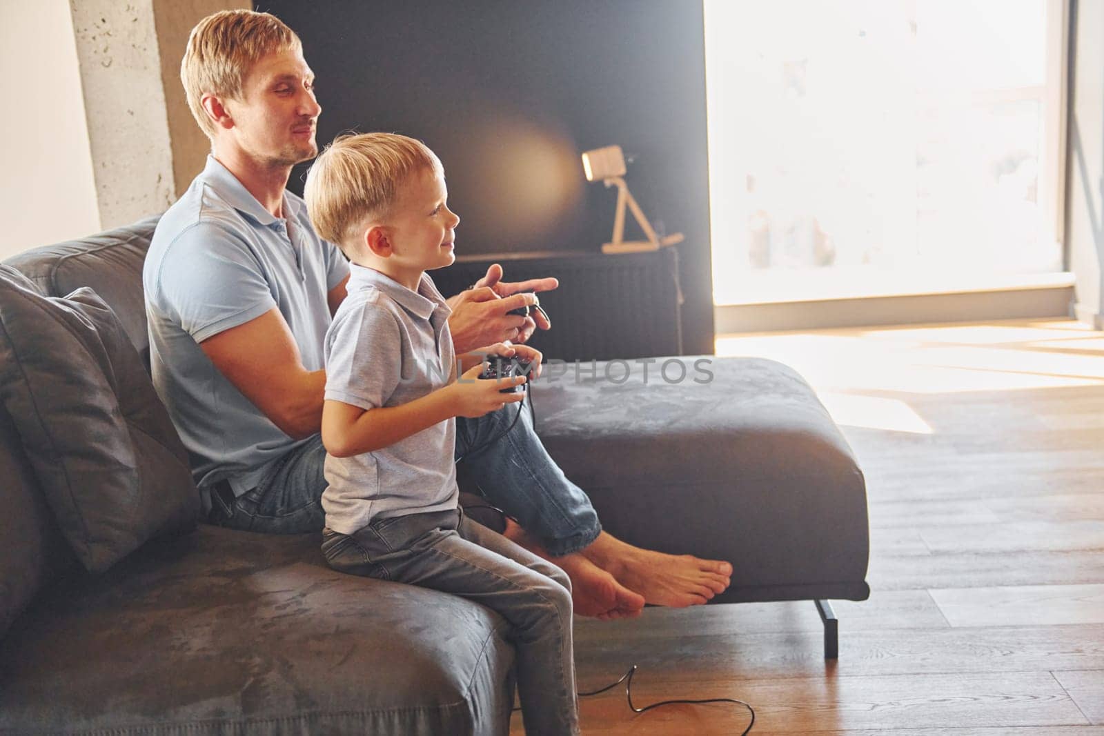 Playing video game. Father and son is indoors at home together.
