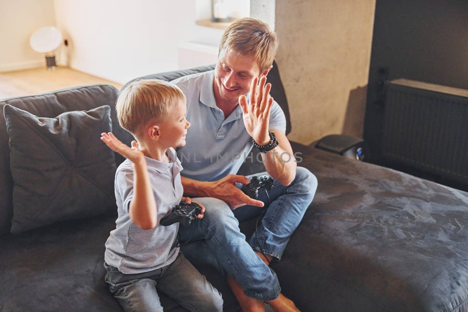Playing video game. Father and son is indoors at home together.