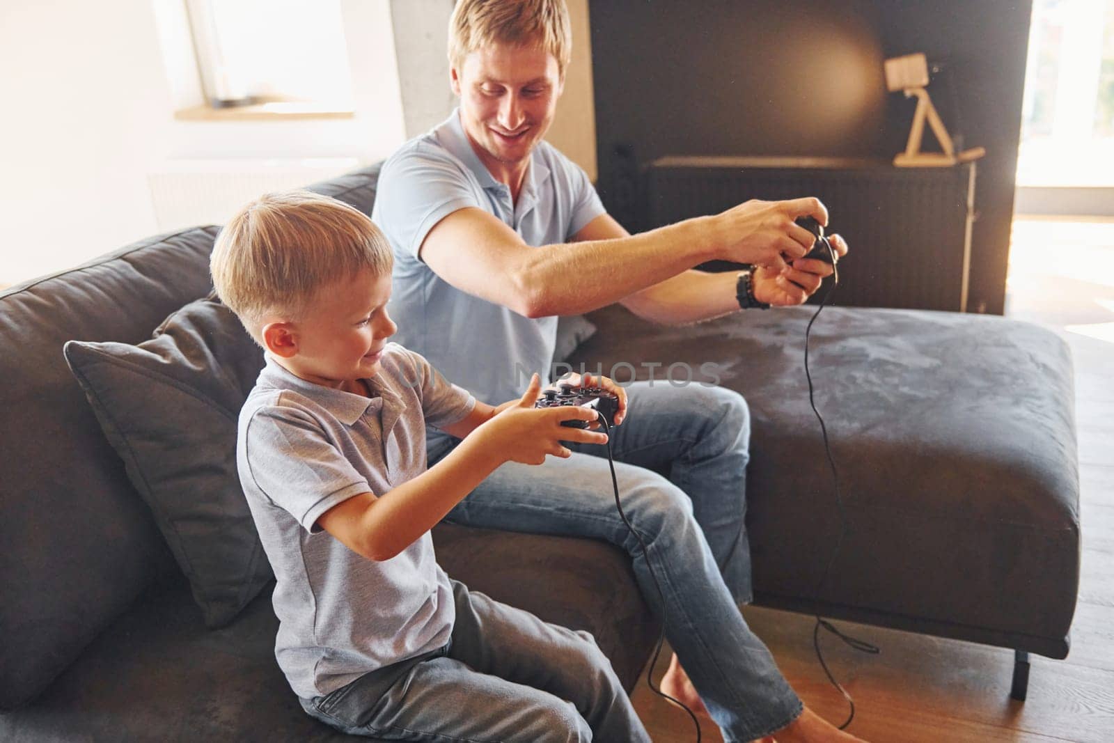 With video game joysticks. Father and son is indoors at home together.