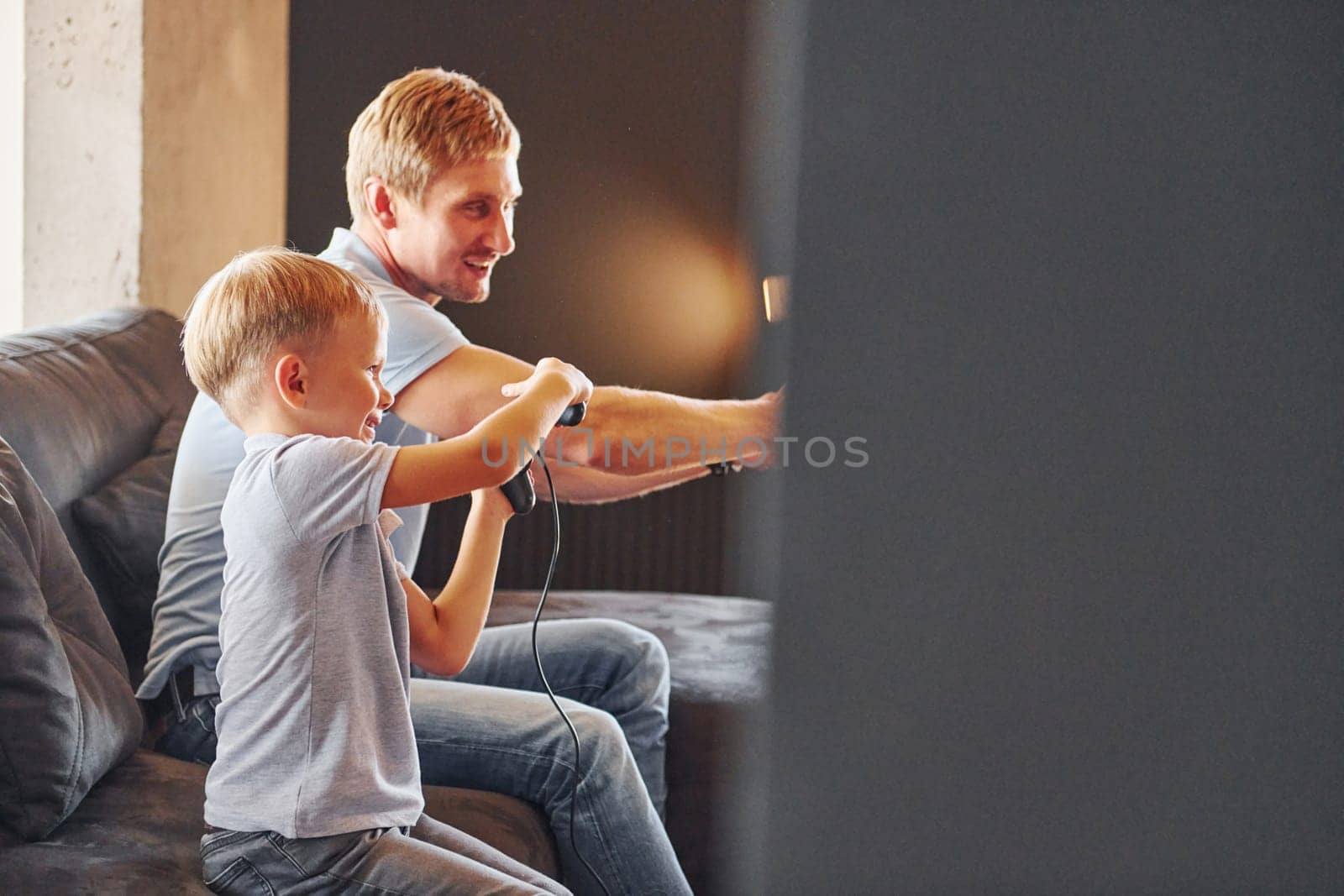 Holding video game controllers. Father and son is indoors at home together.