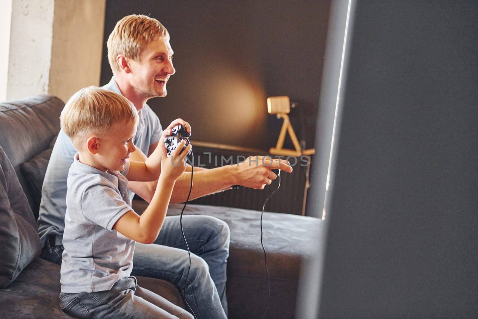 Holding video game controllers. Father and son is indoors at home together.