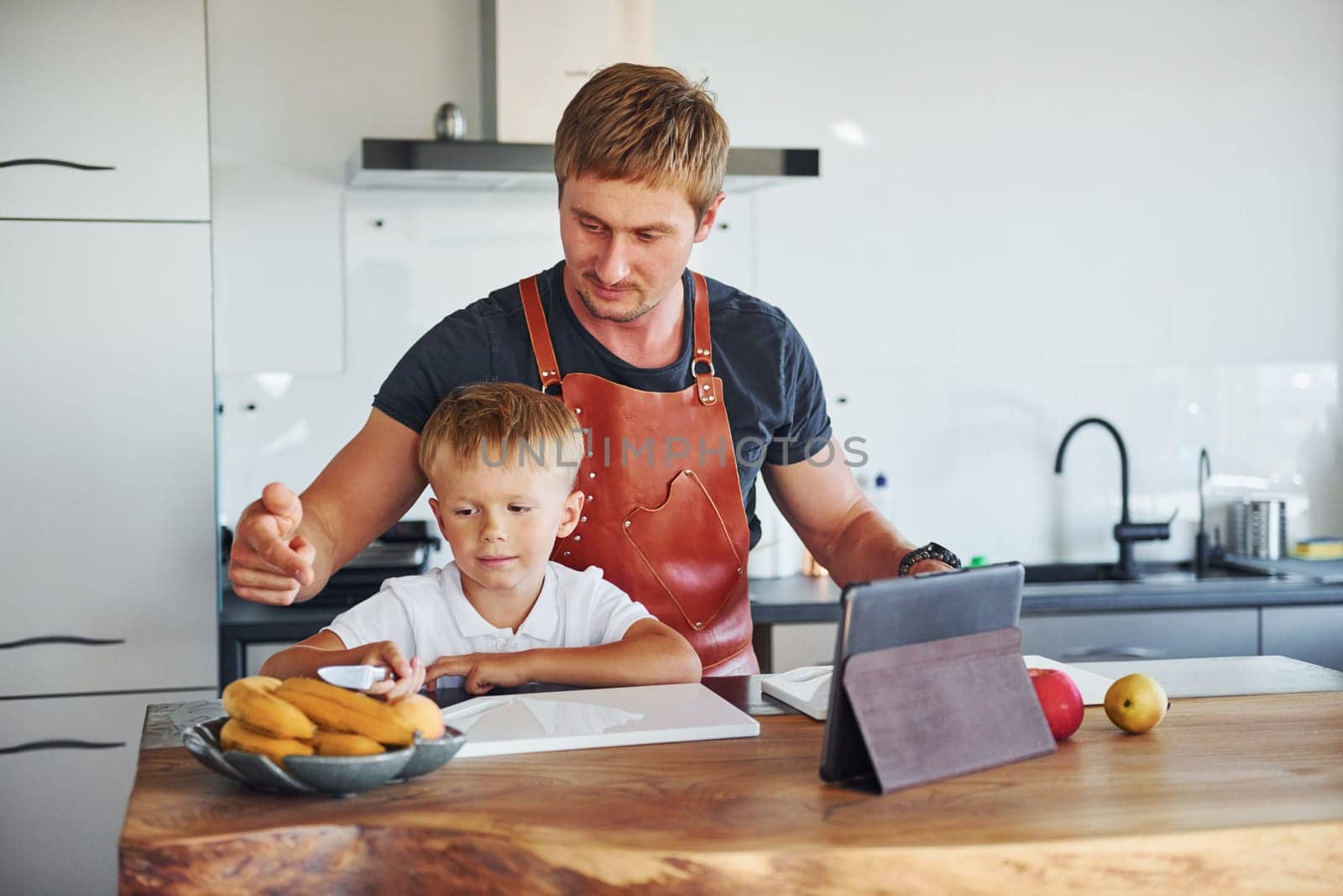 Learning how to cook. Father and son is indoors at home together.