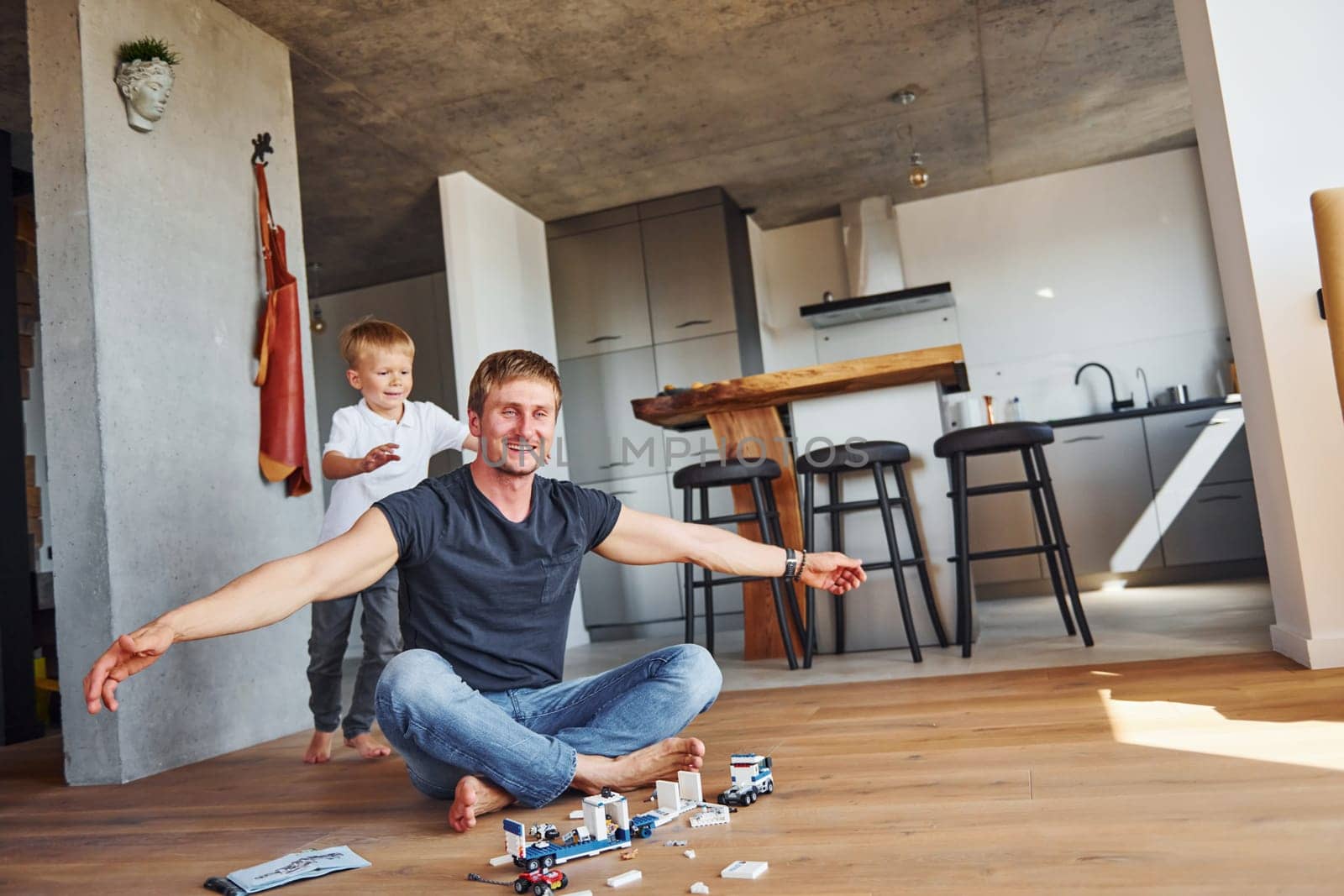 Sitting on the floor and playing with toys. Father and son is indoors at home together by Standret