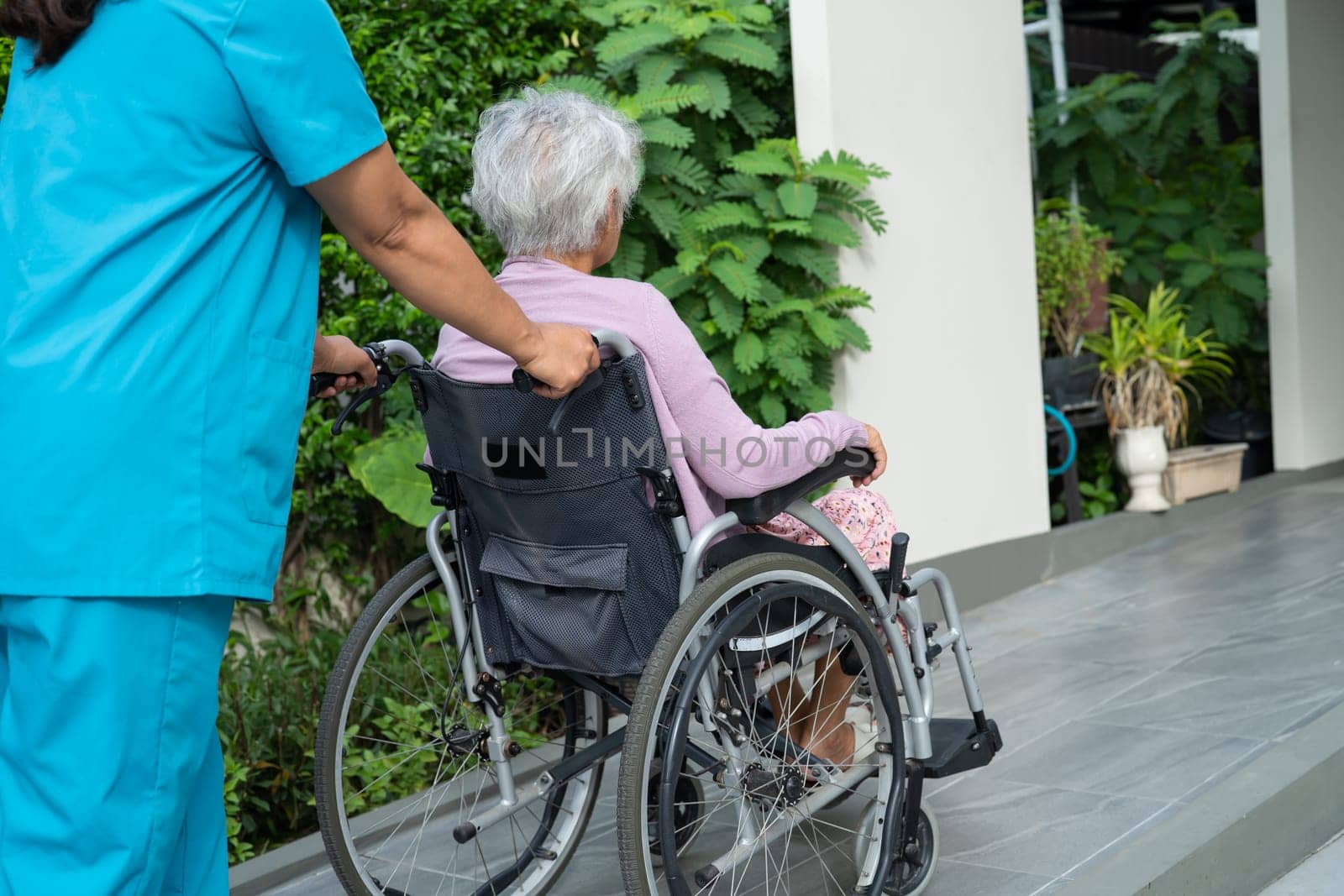 Caregiver help and care Asian senior or elderly old lady woman patient sitting on wheelchair to ramp in nursing hospital, healthy strong medical concept.