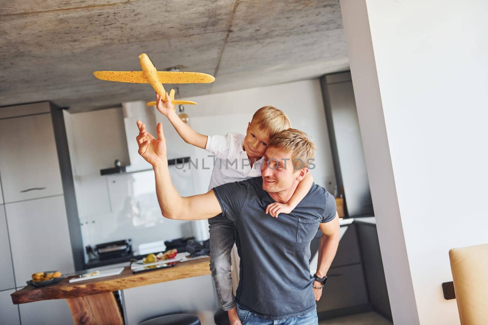 Playing with yellow toy plane. Father and son is indoors at home together by Standret
