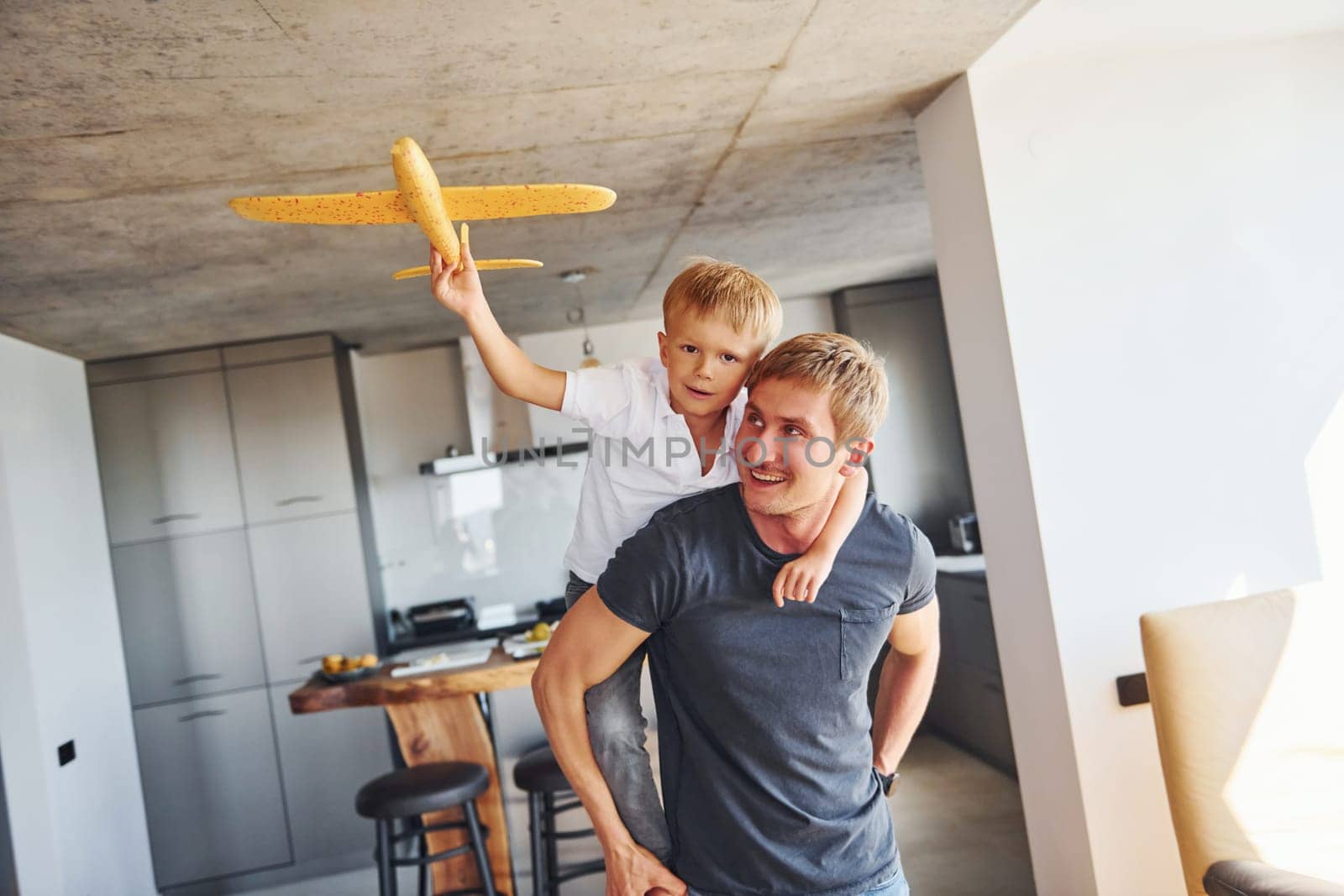 Yellow toy plane. Father and son is indoors at home together by Standret