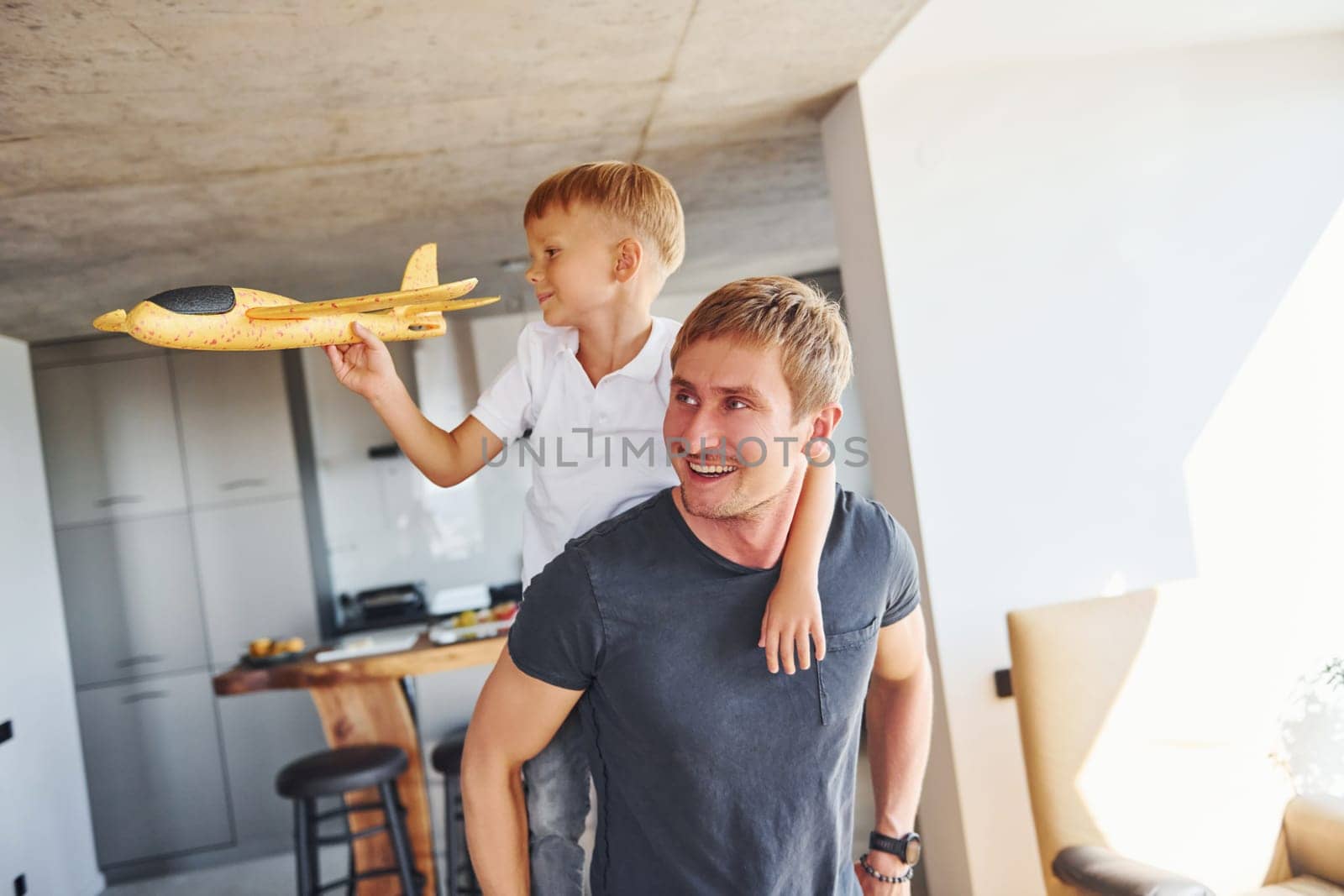 Yellow toy plane. Father and son is indoors at home together.