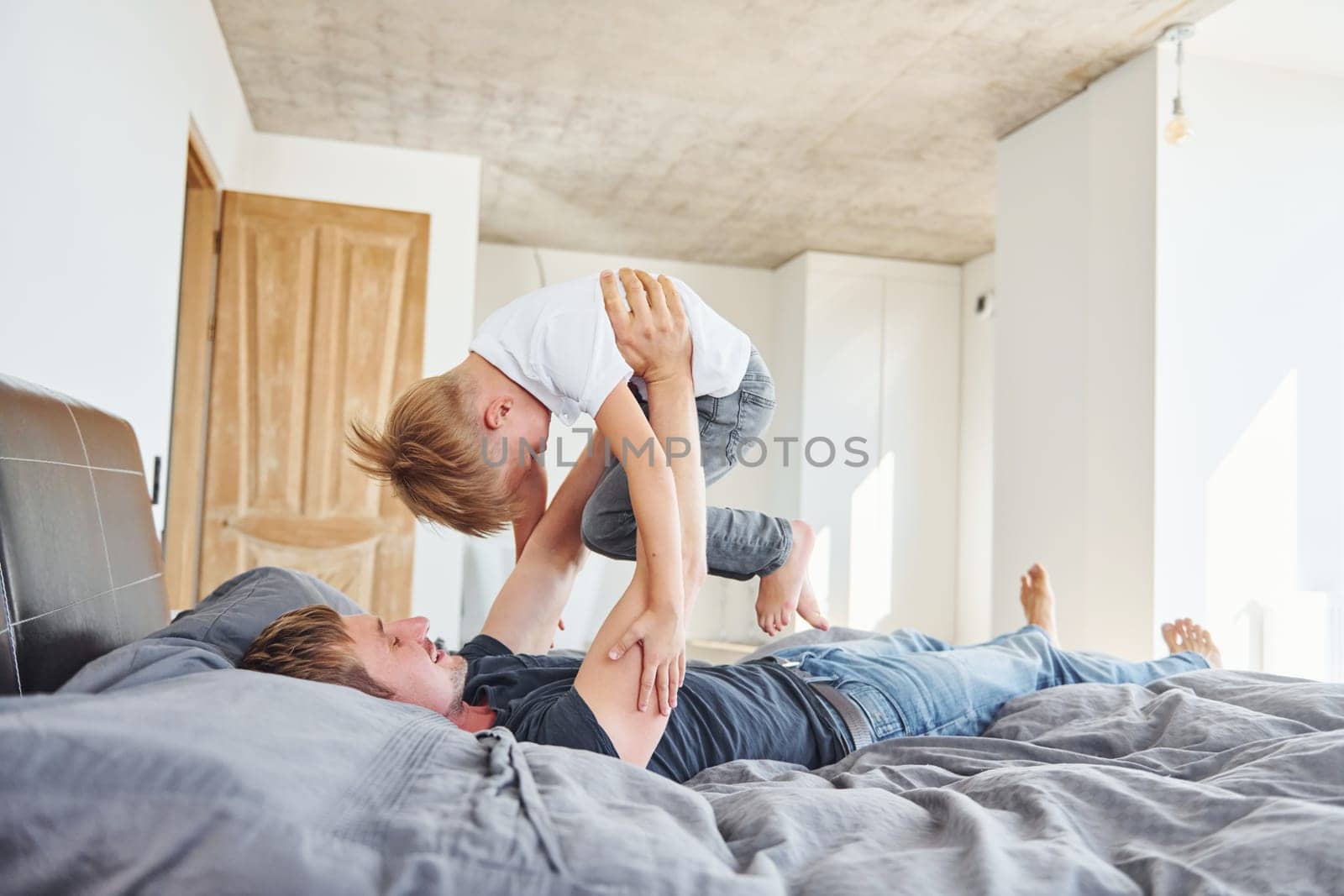 Laying down on the bed. Father and son is indoors at home together.