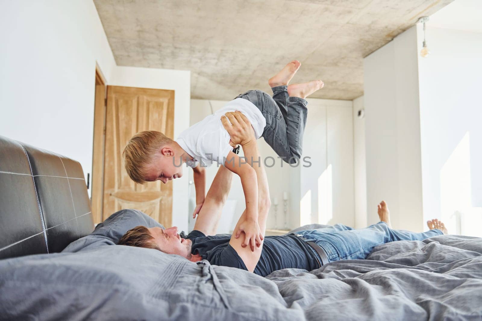 Laying down on the bed. Father and son is indoors at home together.