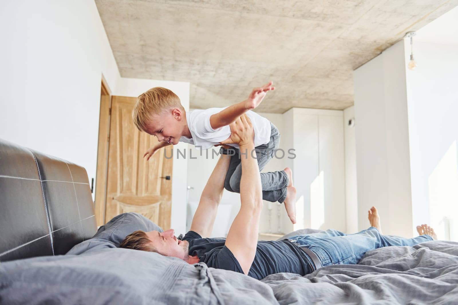 Laying down on the bed. Father and son is indoors at home together.
