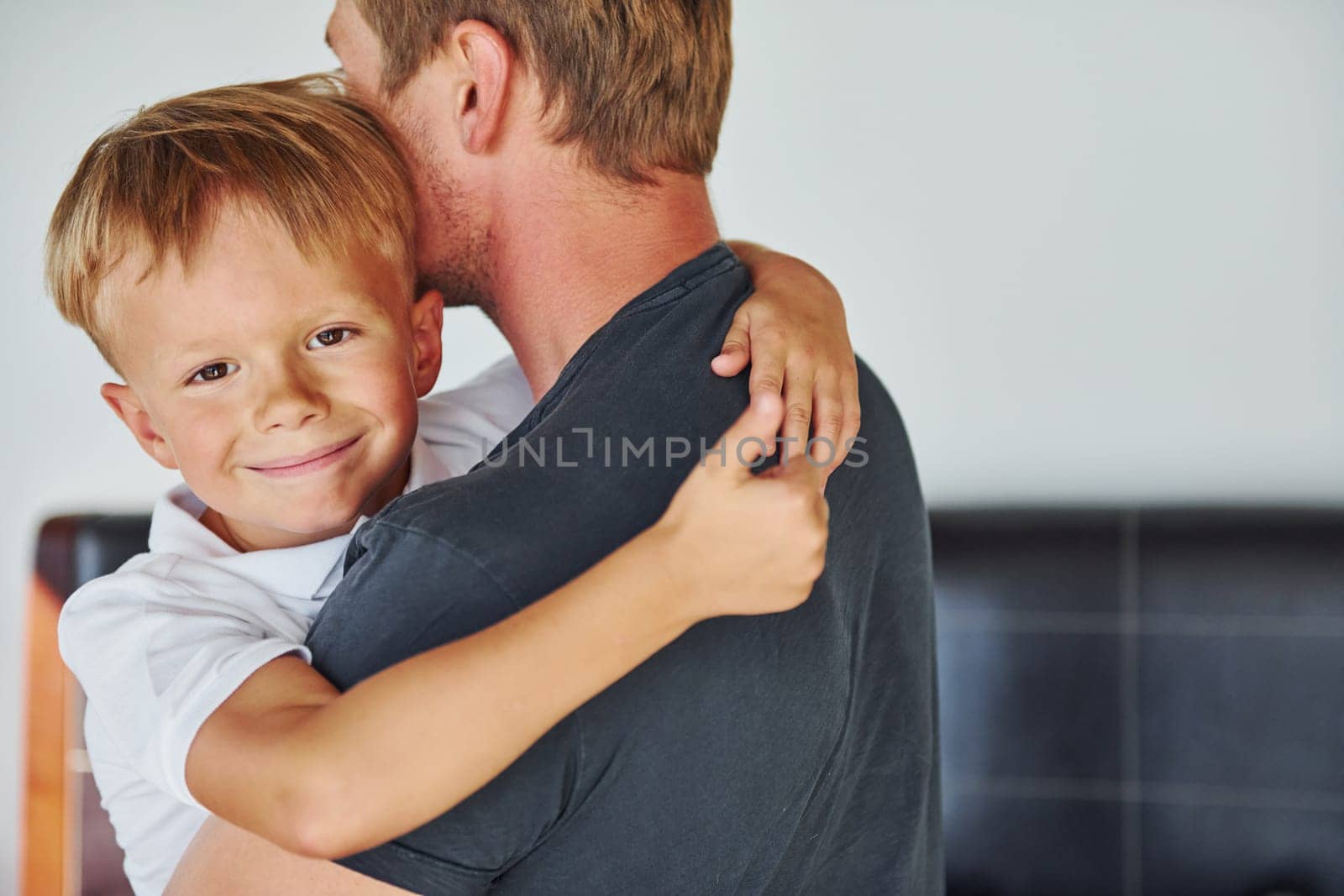 Embracing each other. Father and son is indoors at home together by Standret