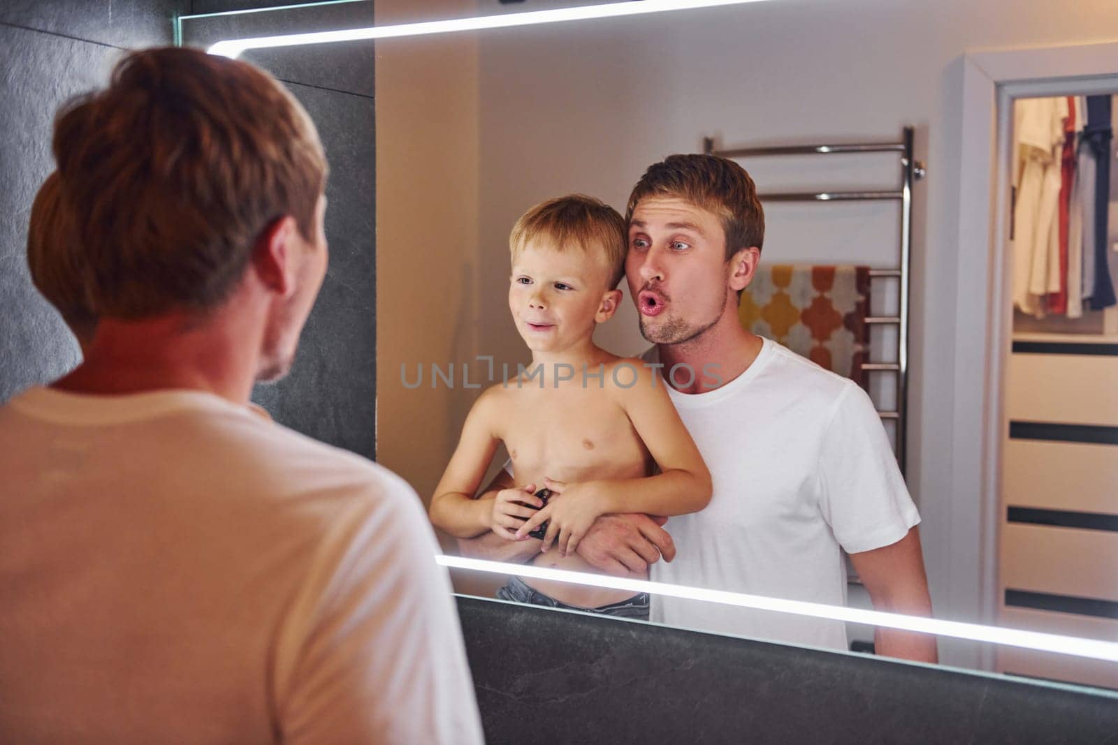 Looking in the mirror in bathroom. Father and son is indoors at home together.