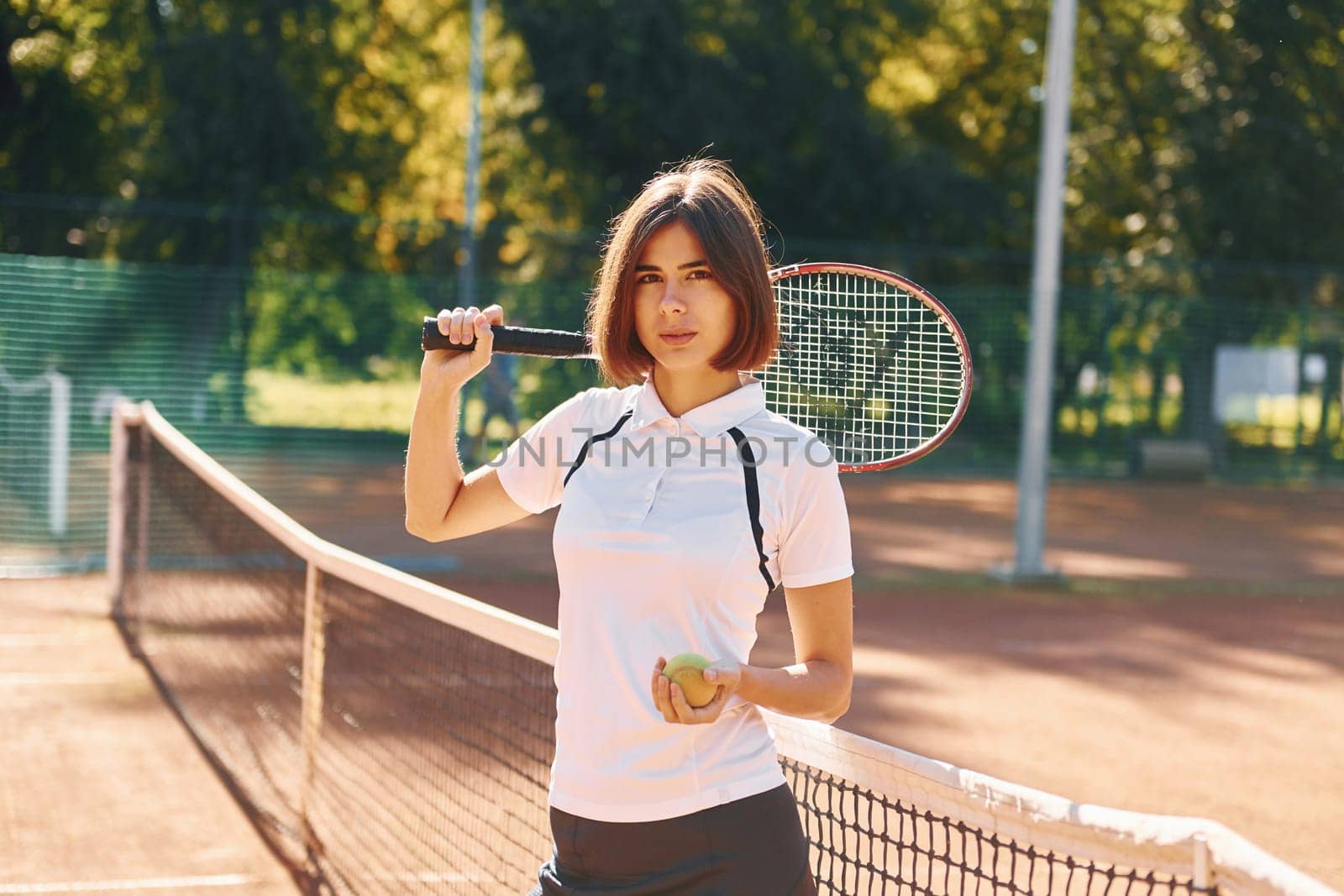 Standing with racket in hand. Female tennis player is on the court at daytime.
