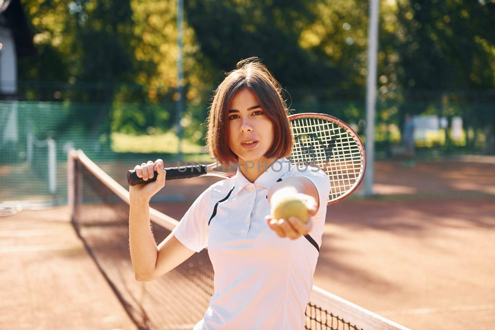 Standing with racket in hand. Female tennis player is on the court at daytime.