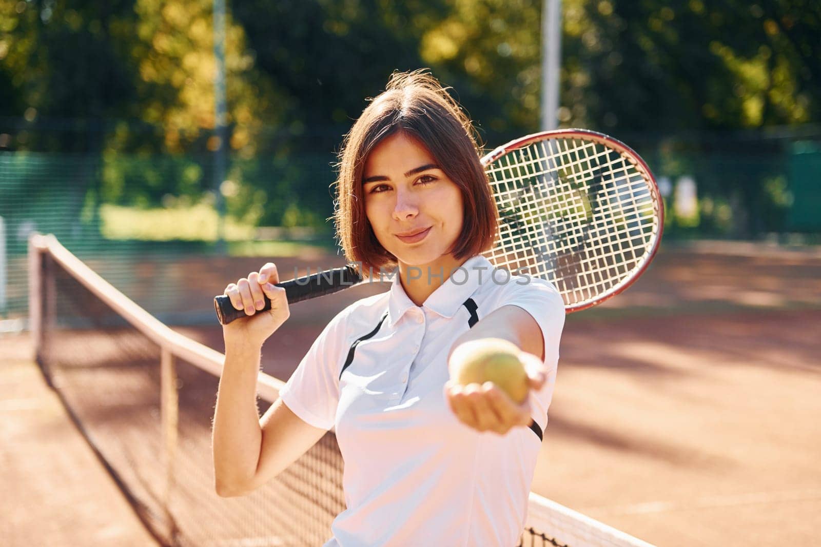 Standing with racket in hand. Female tennis player is on the court at daytime.