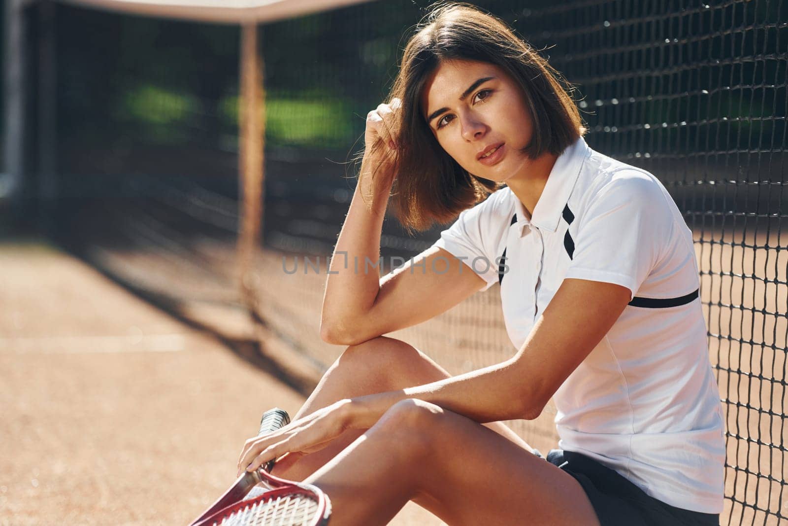 Looking at the camera. Female tennis player is on the court at daytime.