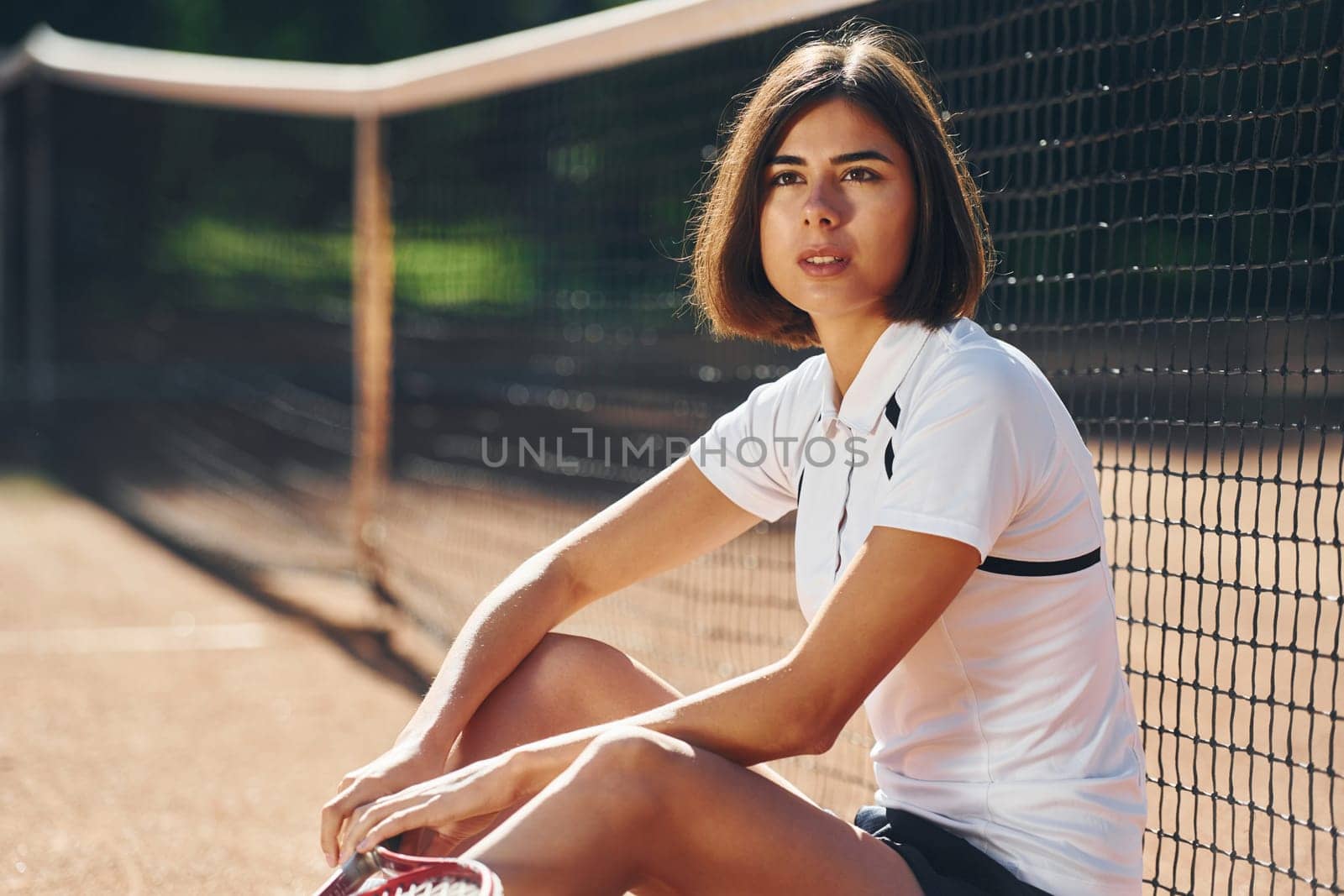 Looking at the camera. Female tennis player is on the court at daytime.