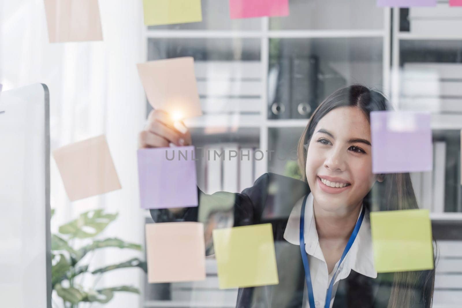 Young businesswoman creative team using post it notes in glass wall to writing strategy business plan to development grow to success...