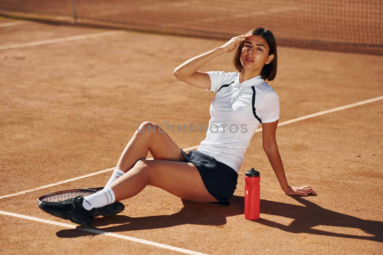 With bottle of water. Female tennis player is on the court at daytime.