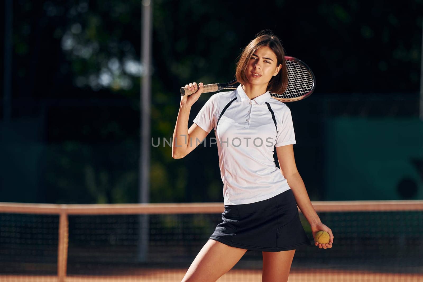 Female tennis player is on the court at daytime posing for a camera.