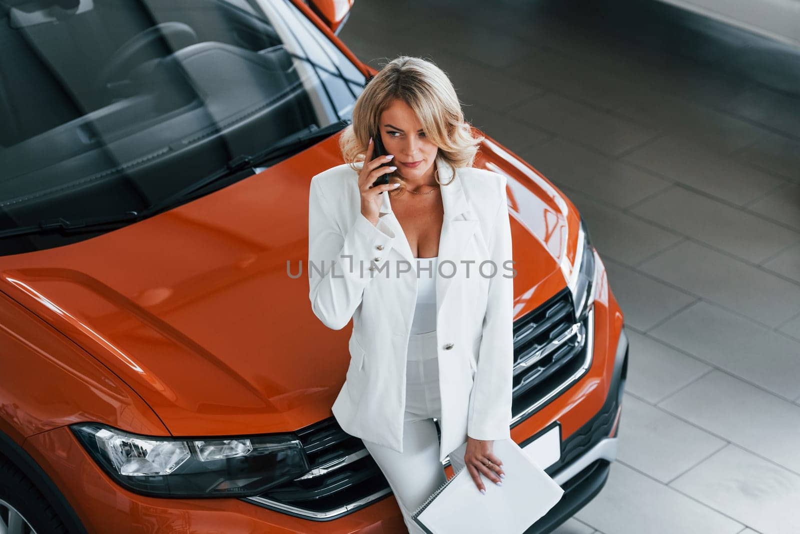 Holding phone. Woman in formal clothes is indoors in the autosalon.