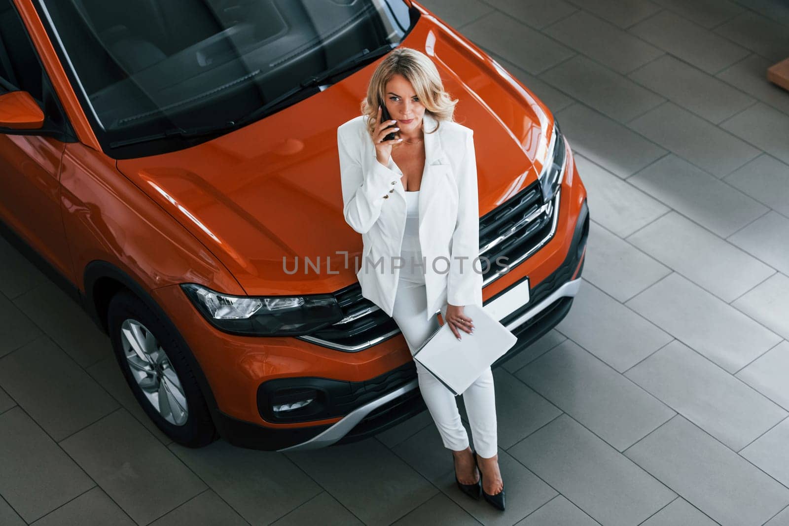 With phone in hand. Woman in formal clothes is indoors in the autosalon.