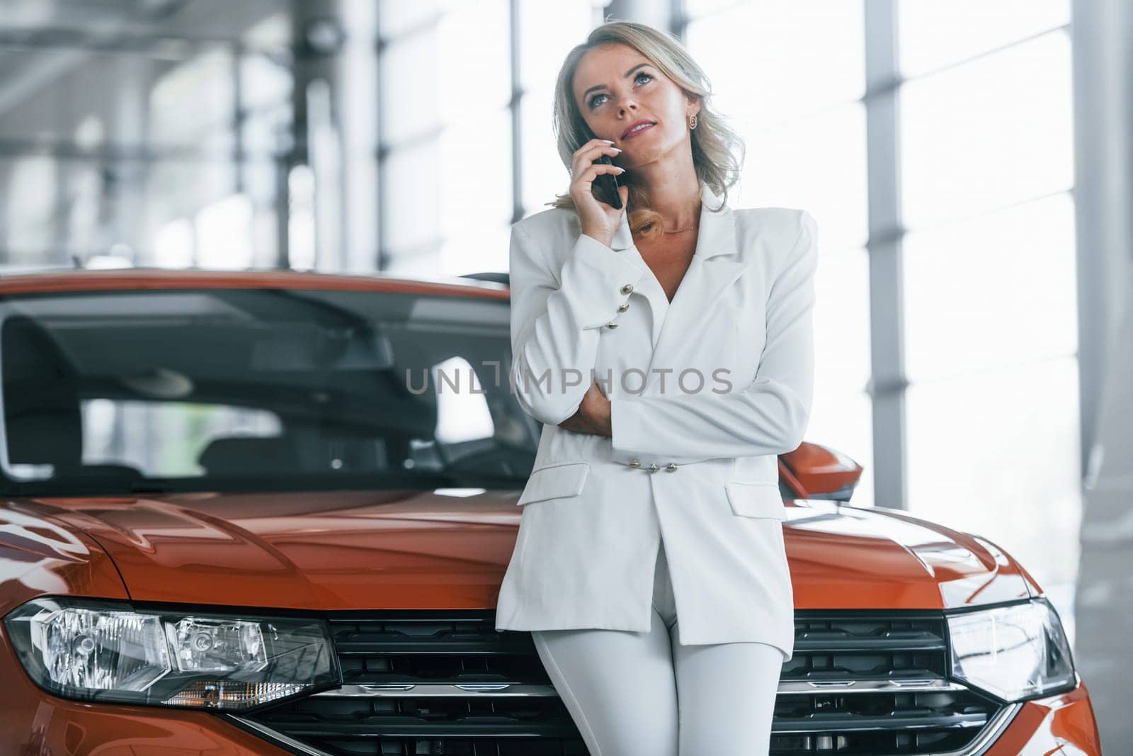 Using phone. Woman in formal clothes is indoors in the autosalon.