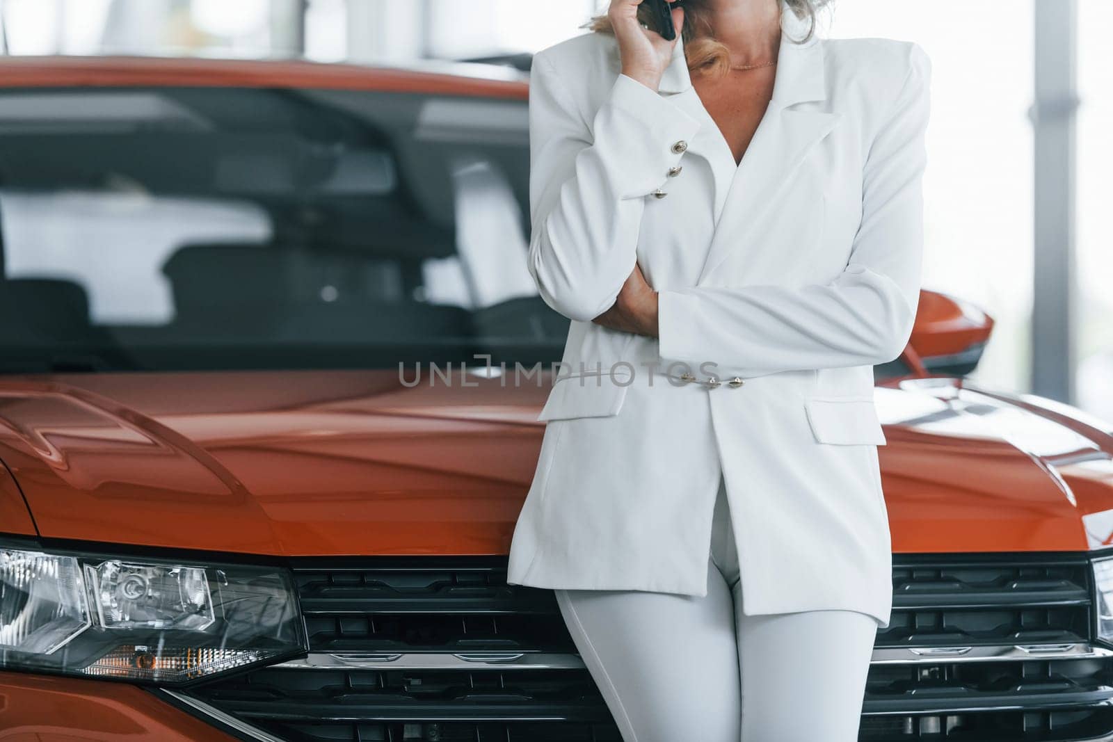 Using phone. Woman in formal clothes is indoors in the autosalon.