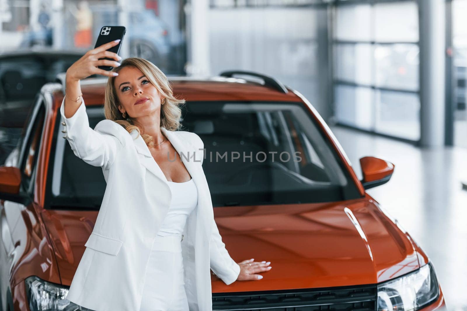 Making selfie. Woman in formal clothes is indoors in the autosalon.