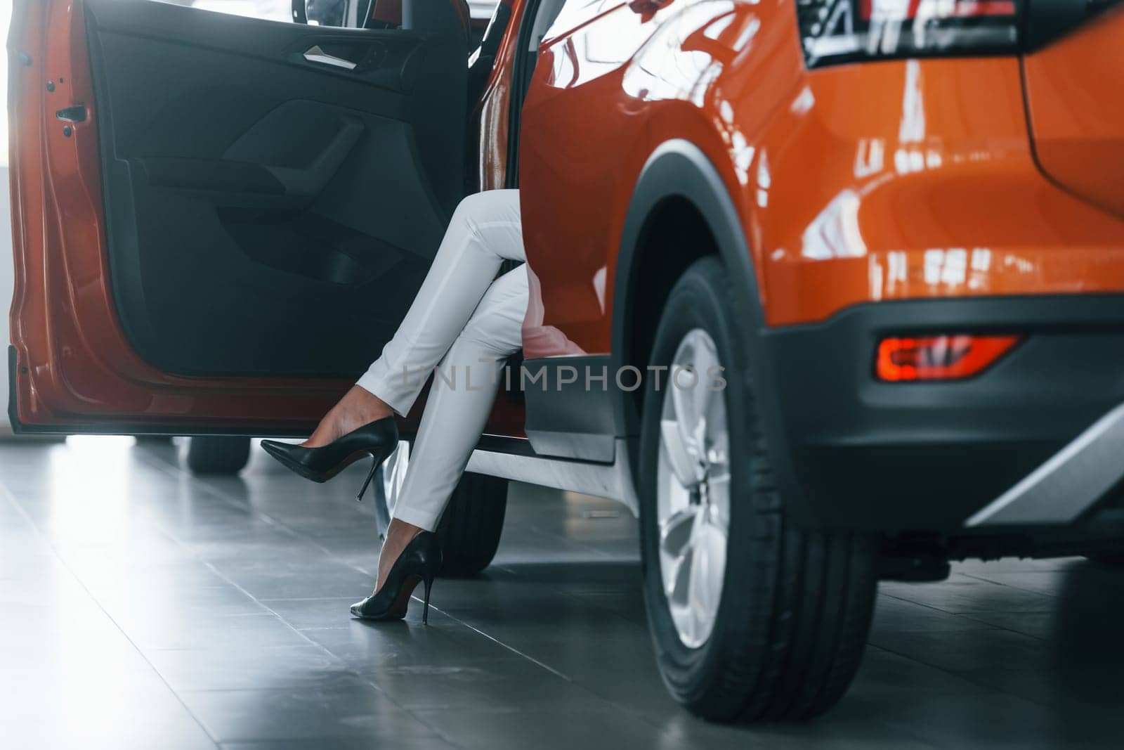 Sitting in the car. Woman in formal clothes is indoors in the autosalon.