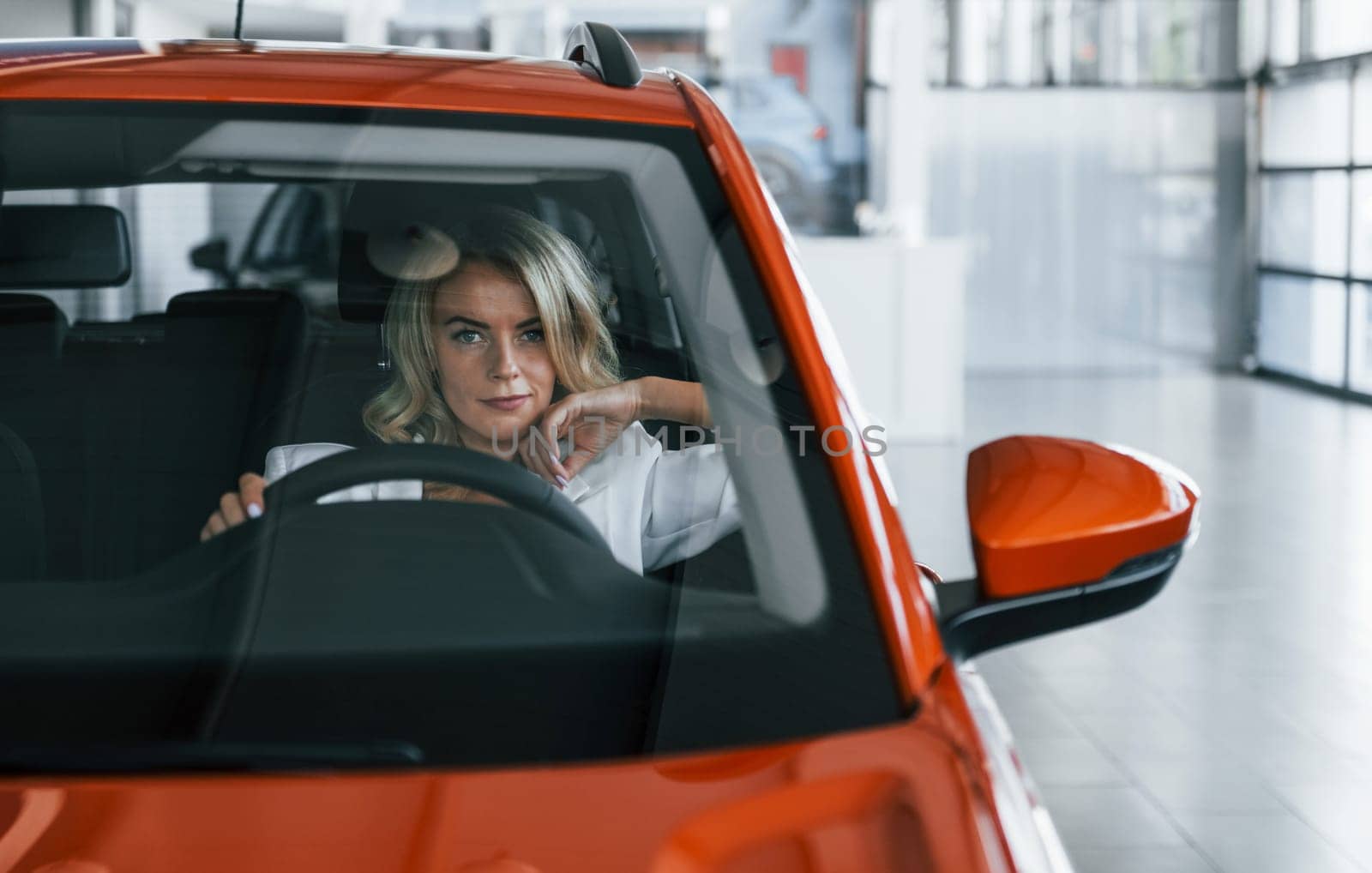 Sitting in the car. Woman in formal clothes is indoors in the autosalon.