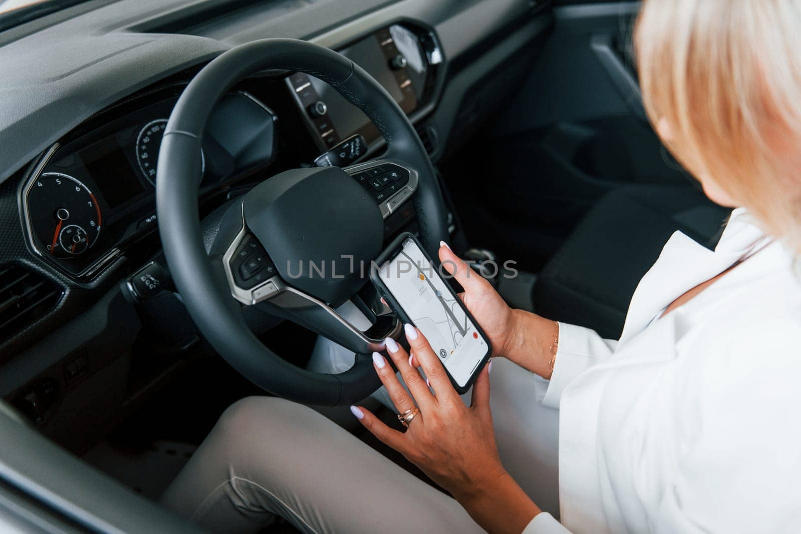 Sitting in the car. Woman in formal clothes is indoors in the autosalon.