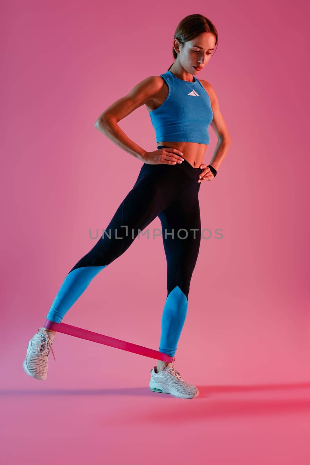 Athletic woman trains legs with fitness elastic band on studio background by Yaroslav_astakhov