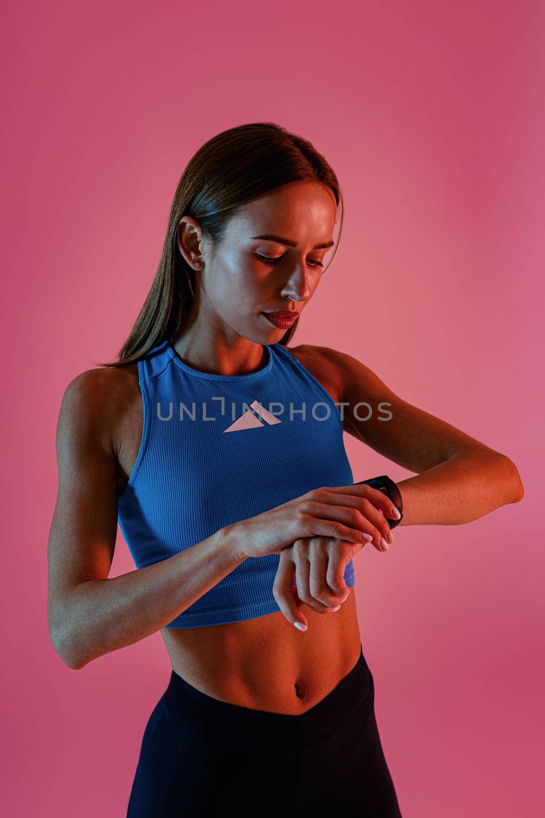 Woman standing and looking at smartwatch checking her performance on studio background