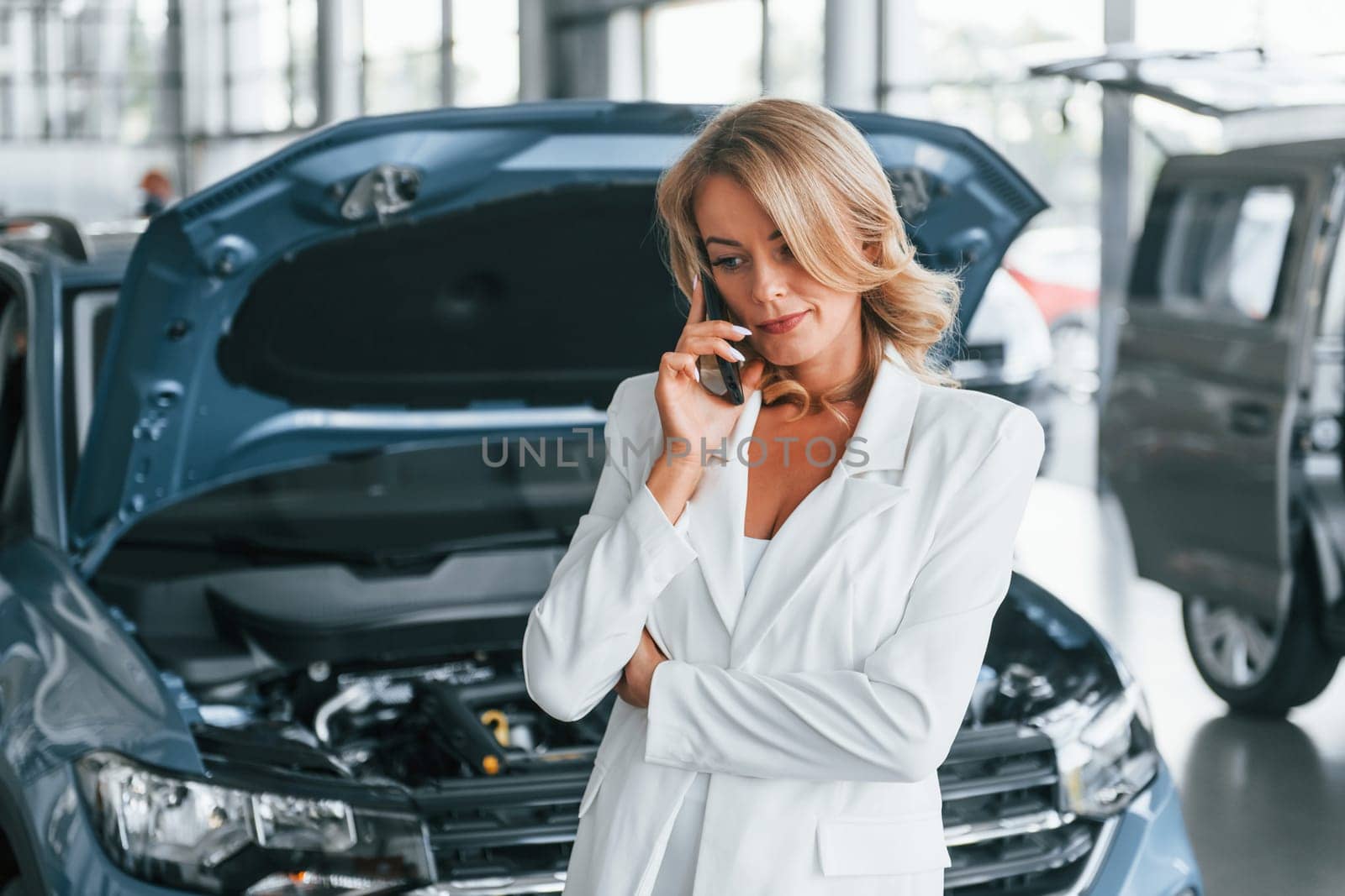 Talking by phone. Woman in formal clothes is indoors in the autosalon.