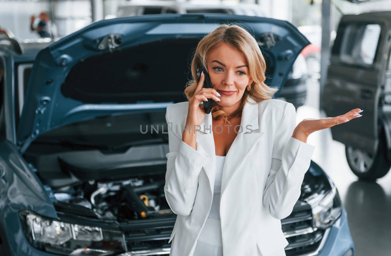 Talking by phone. Woman in formal clothes is indoors in the autosalon.