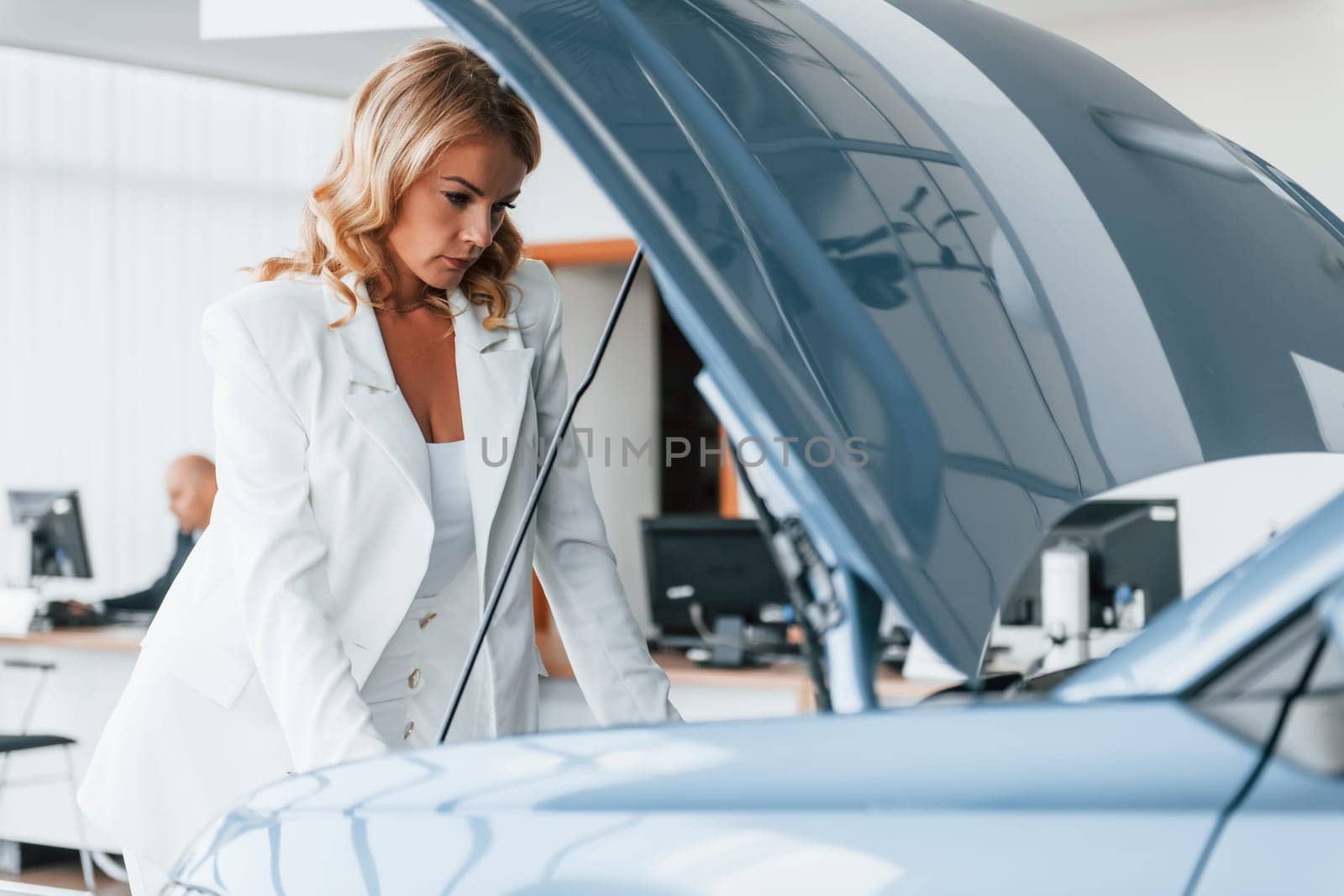 Under the car hood. Woman in formal clothes is indoors in the autosalon.