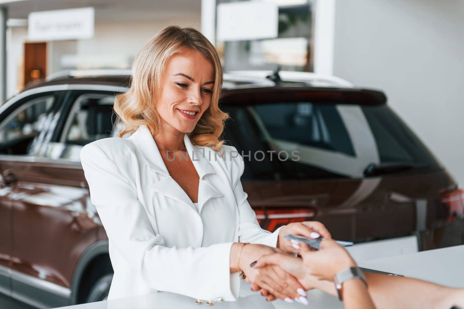 Paying for the product. Woman in formal clothes is indoors in the autosalon.