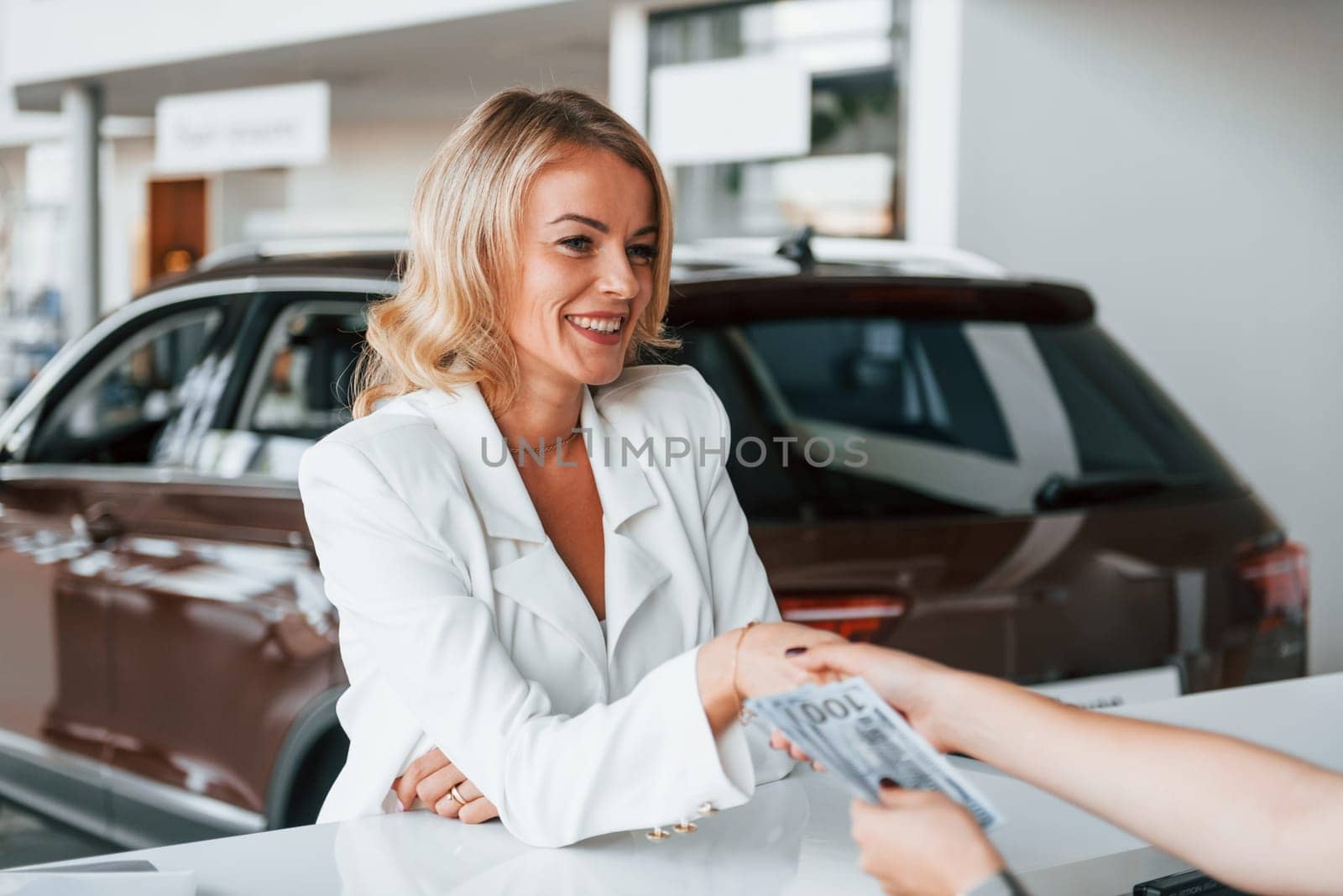 Paying for the product. Woman in formal clothes is indoors in the autosalon.
