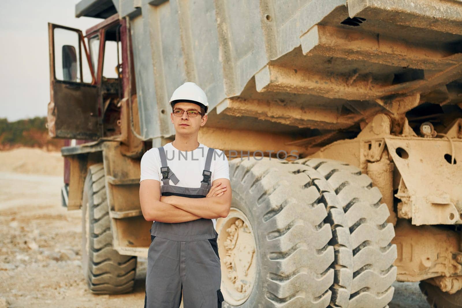 Near loading vehicle. Worker in professional uniform is on the borrow pit at daytime.