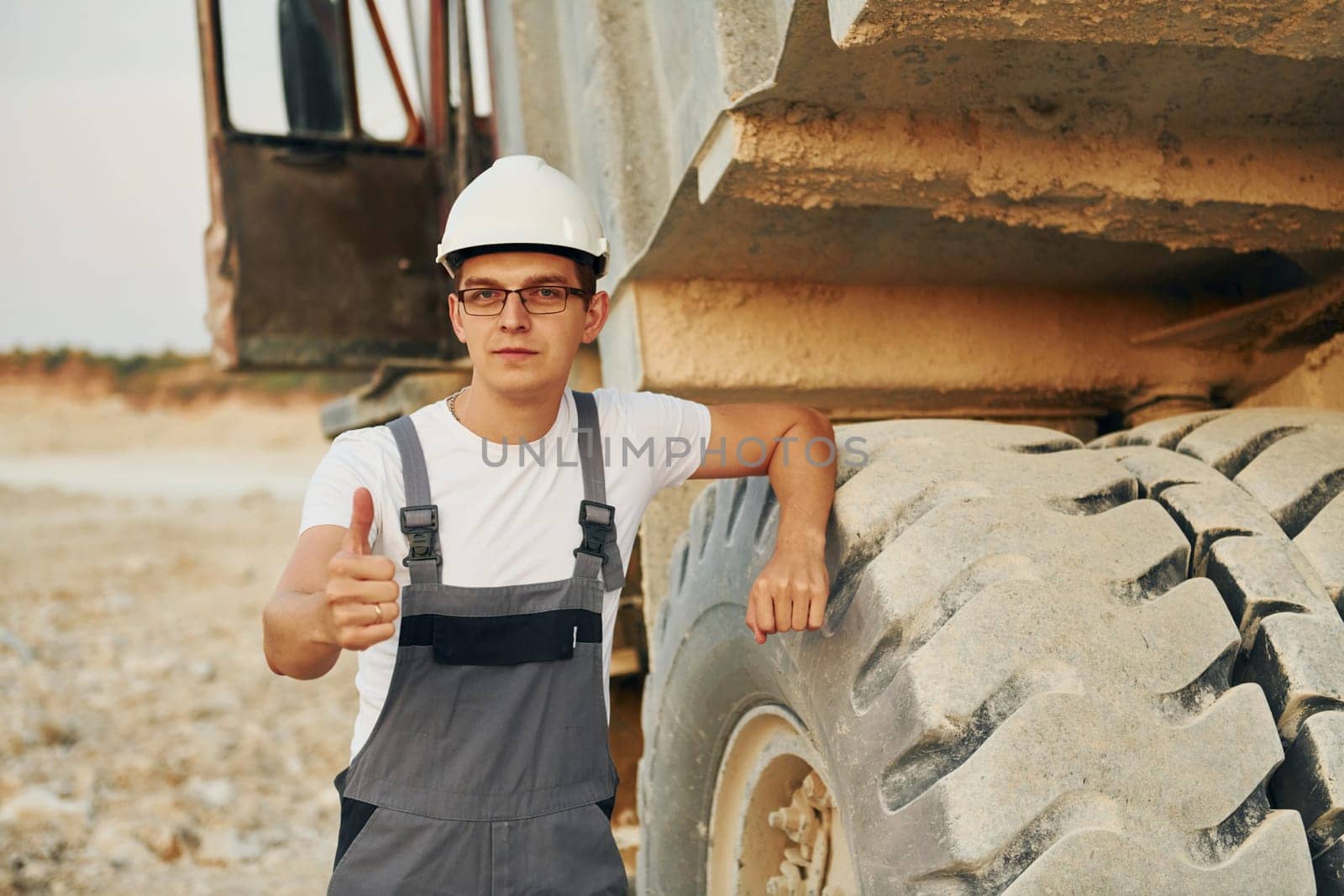 Near loading vehicle. Worker in professional uniform is on the borrow pit at daytime.