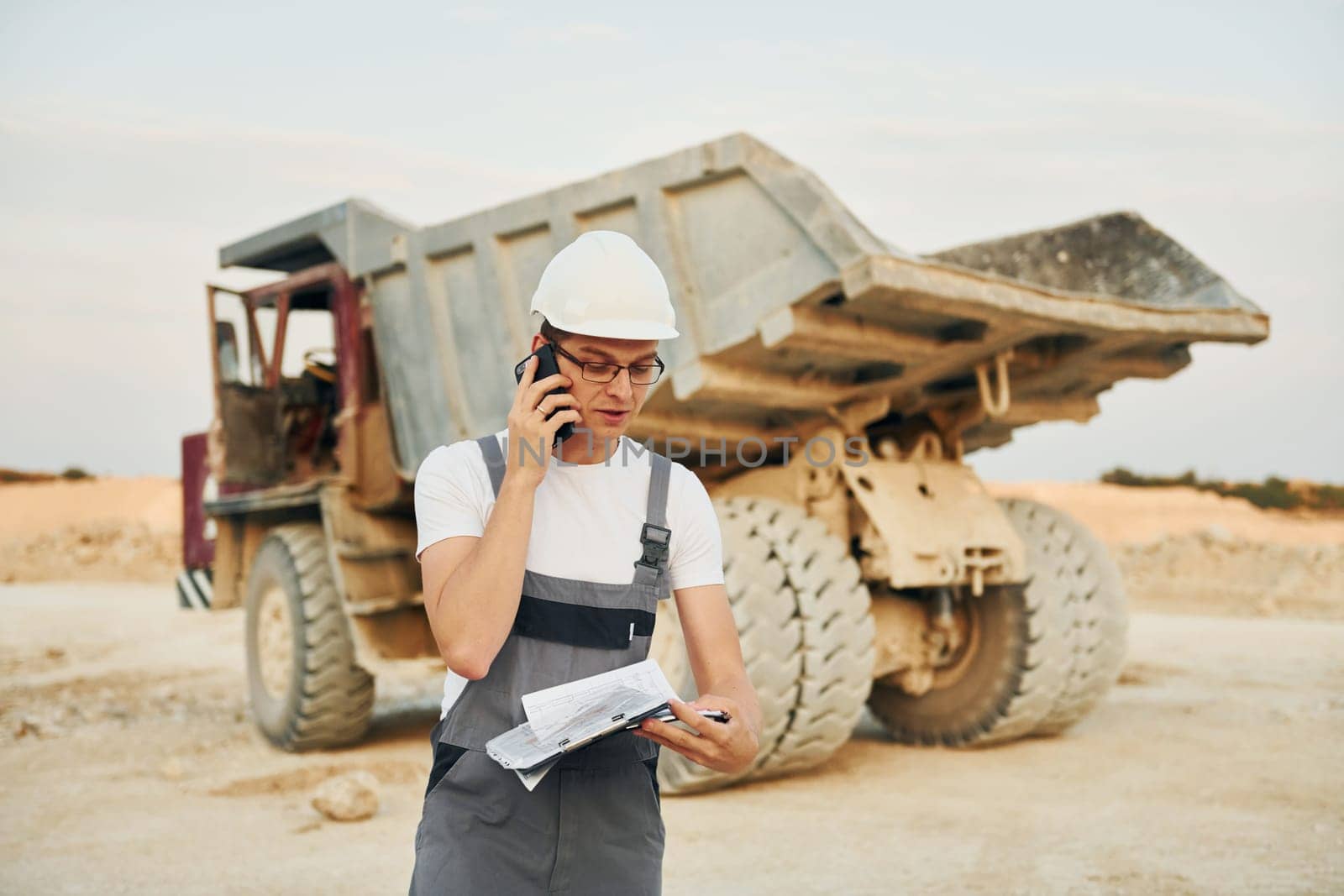 In white hard hat. Worker in professional uniform is on the borrow pit at daytime.