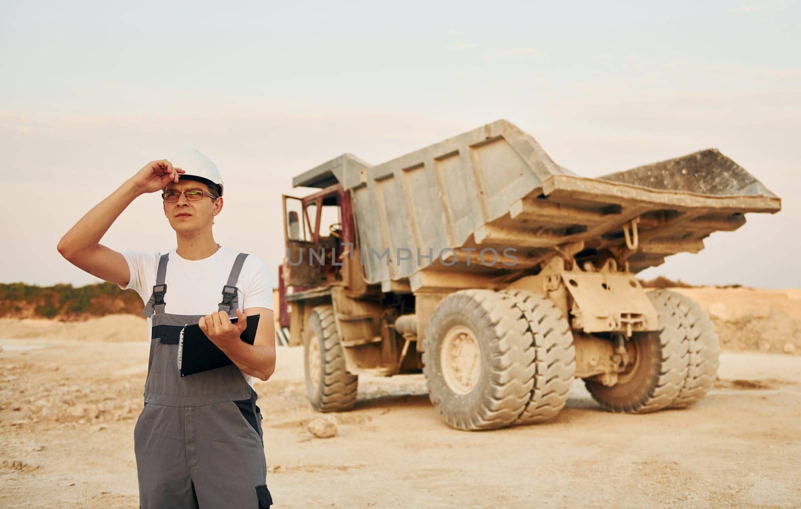In white hard hat. Worker in professional uniform is on the borrow pit at daytime.
