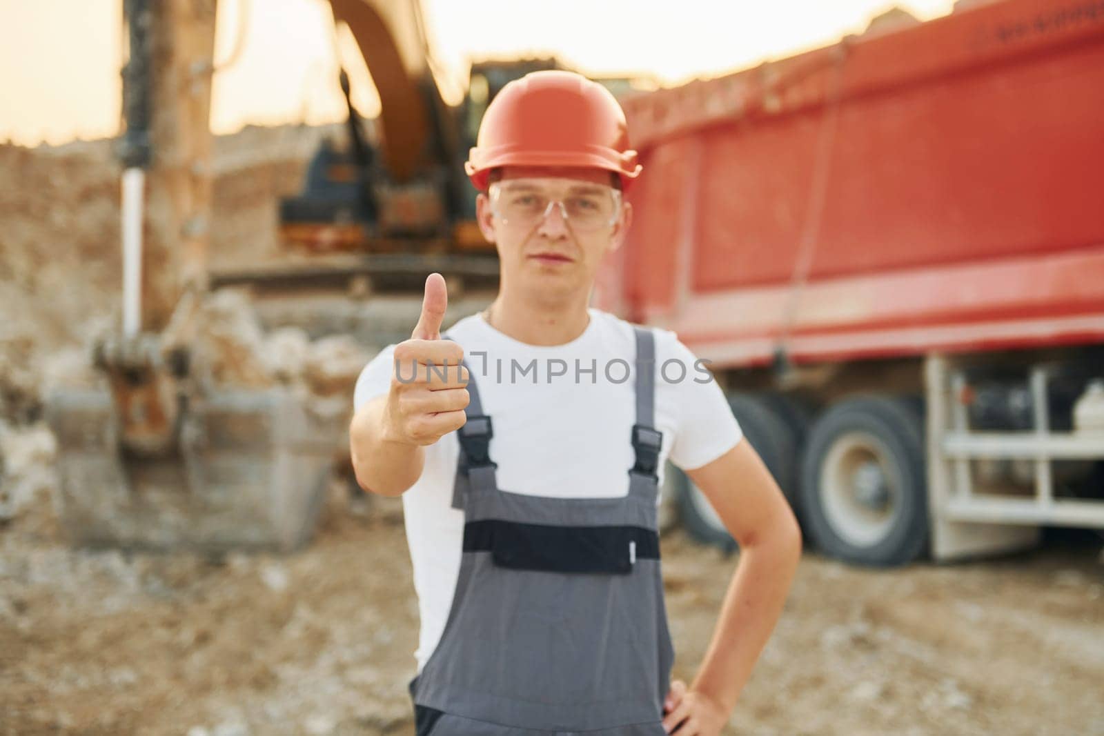 In front of vehicle. Worker in professional uniform is on the borrow pit at daytime.