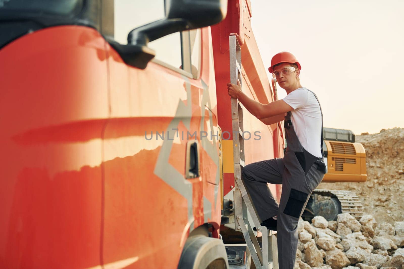 Going up to the vehicle seat. Worker in professional uniform is on the borrow pit at daytime.