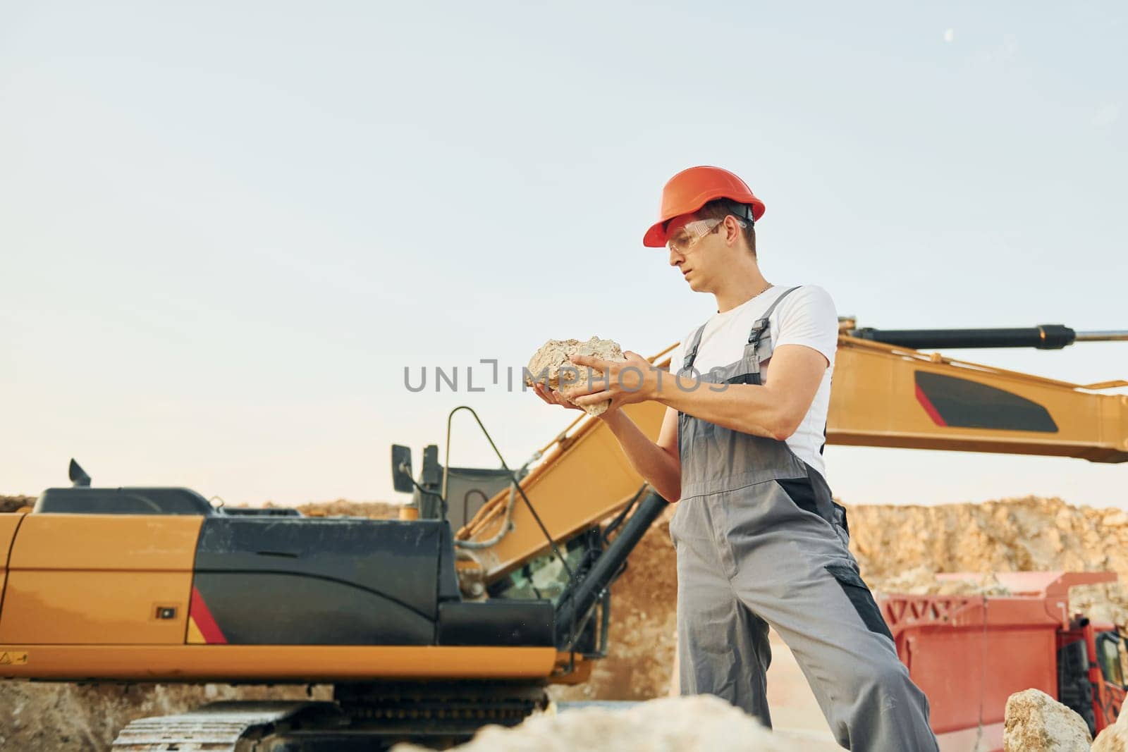 Holding documents in hands. Worker in professional uniform is on the borrow pit at daytime.
